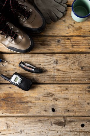 Photo for Camping equipment of trekking shoes, metal cup, walkie talkie on wooden background with copy space. National camping month, equipment and celebration concept. - Royalty Free Image