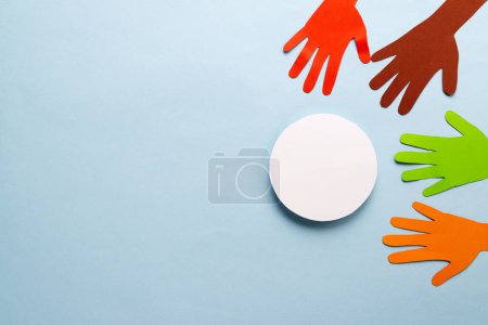 Photo for Paper cut out of multi coloured hands and white circle with copy space on blue background. Humanitarian aid, people, help and human concept. - Royalty Free Image