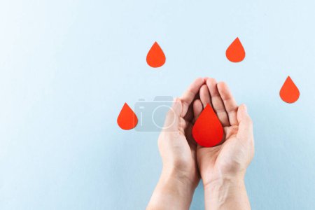 Photo for Hands of caucasian woman cupping blood drop, with blood drops on blue background, copy space. Blood donation, medicine and healthcare. - Royalty Free Image