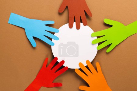 Foto de Papel cortado de manos multicolores y círculo blanco con espacio de copia sobre fondo marrón. Ayuda humanitaria, personas, ayuda y concepto humano. - Imagen libre de derechos
