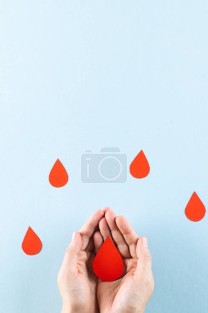 Foto de Manos de mujer caucásica tomando gota de sangre, con gotas de sangre sobre fondo azul, espacio para copiar. Donación de sangre, medicamentos y asistencia sanitaria. - Imagen libre de derechos