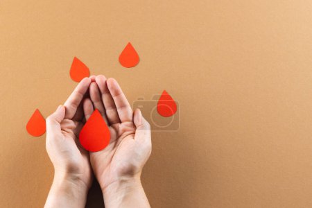 Photo for Hands of caucasian woman cupping blood drop, with blood drops on brown background, copy space. Blood donation, medicine and healthcare. - Royalty Free Image