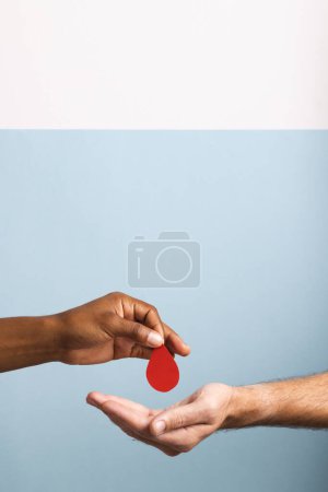Téléchargez les photos : Mains de l'homme biracial donnant goutte de sang à l'homme caucasien, sur fond bleu et blanc, copier l'espace. Don de sang, médicaments et soins de santé. - en image libre de droit