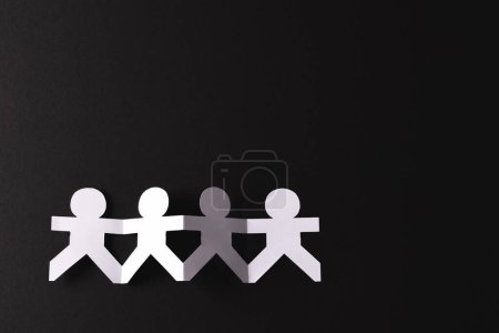 Photo for Close up of four paper cut out people figures holding hands with copy space on black background. Humanitarian, people, help and human concept. - Royalty Free Image
