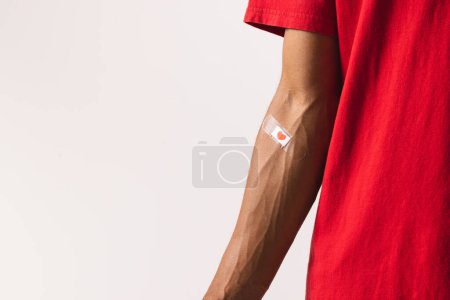Photo for Midsection of biracial man with heart sticking plaster on arm, on white background with copy space. Blood donation, medicine and healthcare. - Royalty Free Image