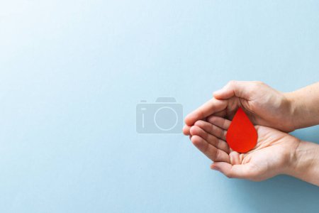 Téléchargez les photos : Mains de femme caucasienne coupant goutte de sang, sur fond bleu avec espace de copie. Don de sang, médicaments et soins de santé. - en image libre de droit