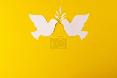 Téléchargez les photos : Gros plan de deux colombes blanches avec feuille et espace de copie sur fond jaune. Concept de mouvement pour la paix et contre la guerre. - en image libre de droit