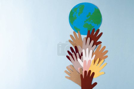 Photo for Paper cut out of multi coloured hands with globe and copy space on blue background. Humanitarian aid, people, help and human concept. - Royalty Free Image