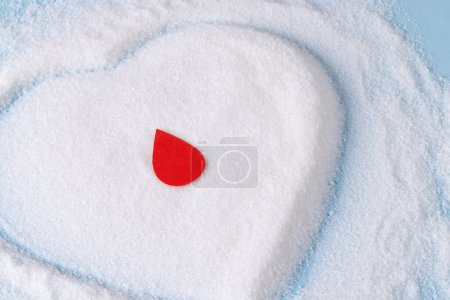 Téléchargez les photos : Goutte de sang sur le sucre en forme de coeur sur fond bleu. Régime alimentaire, glycémie, diabète et santé cardiaque. - en image libre de droit