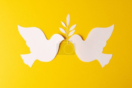 Téléchargez les photos : Gros plan de deux colombes blanches avec feuille et espace de copie sur fond jaune. Concept de mouvement pour la paix et contre la guerre. - en image libre de droit