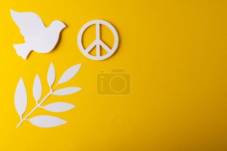 Photo for High angle view of white peace sign, white dove and leaf with copy space on yellow background. Peace and anti war movement concept. - Royalty Free Image