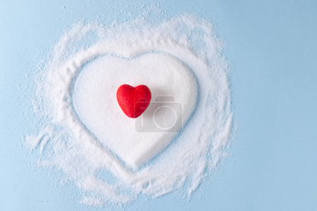 Photo for Red heart over sugar in heart shape on blue background. Diet, blood sugar, diabetes and heart health awareness. - Royalty Free Image