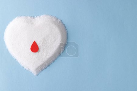 Foto de Gota de sangre sobre el azúcar en forma de corazón sobre fondo azul con espacio para copiar. Dieta, azúcar en sangre, diabetes y conciencia de la salud del corazón. - Imagen libre de derechos