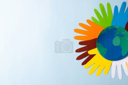 Photo for Paper cut out of multi coloured hands and globe with copy space on blue background. Humanitarian aid, people, help and human concept. - Royalty Free Image