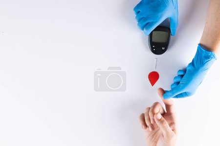 Hands of gloved doctor with glucometer taking blood sugar reading from caucasian woman, copy space. Blood sugar, diabetes and health awareness.
