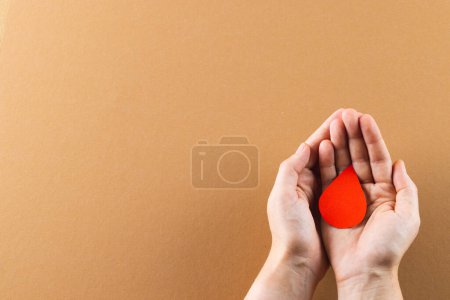 Téléchargez les photos : Mains de femme caucasienne coupant goutte de sang sur fond brun avec espace de copie. Don de sang, médicaments et soins de santé. - en image libre de droit