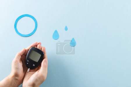 Photo for Hands of caucasian woman holding glucometer over blue drops and ring on blue background, copy space. Blood sugar, diabetes and health awareness. - Royalty Free Image