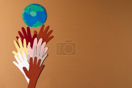 Photo for Paper cut out of multi coloured hands and globe with copy space on brown background. Humanitarian aid, people, help and human concept. - Royalty Free Image