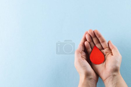 Photo for Hands of caucasian woman cupping blood drop on blue background with copy space. Blood donation, medicine and healthcare. - Royalty Free Image