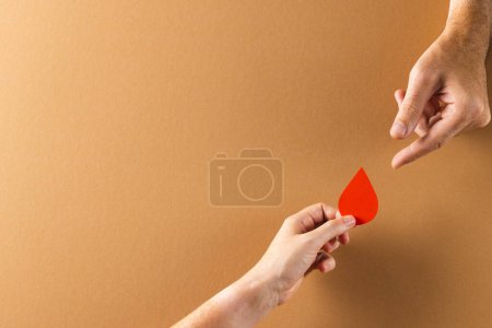 Photo for Hands of caucasian woman passing blood drop to caucasian man, on brown background with copy space. Blood donation, medicine and healthcare. - Royalty Free Image