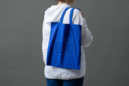 Téléchargez les photos : Femme blanche tenant au-dessus de l'épaule sac en toile bleue avec espace de copie sur fond gris. Sacs et concept de mode. - en image libre de droit