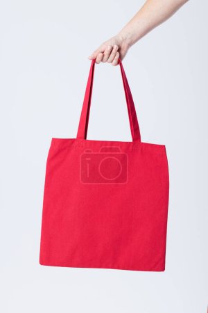 Téléchargez les photos : Main de femme caucasienne tenant sac en toile rouge avec espace de copie sur fond blanc. Sacs et concept de mode. - en image libre de droit