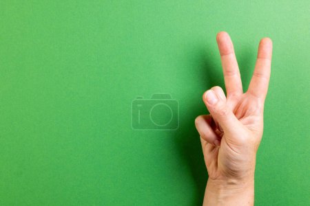 Photo for Close up of hand of caucasian woman showing peace sign with copy space on green background. Peace and anti war movement concept. - Royalty Free Image
