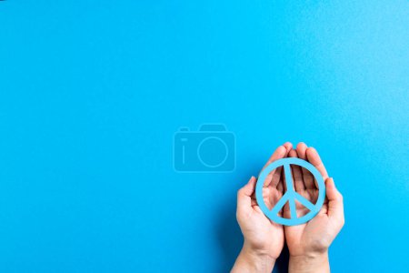 Téléchargez les photos : Gros plan des mains de la femme caucasienne tenant signe de paix avec espace de copie sur fond bleu. Concept de mouvement pour la paix et contre la guerre. - en image libre de droit