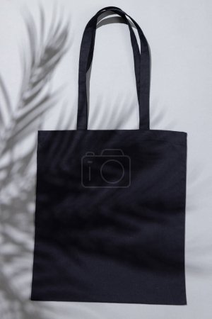 Photo for High angle view of black canvas bag with copy space and leaf shadow on grey background. Bags and fashion concept. - Royalty Free Image