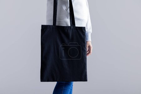 Foto de Mujer caucásica sosteniendo bolsa de lona negra con espacio para copiar sobre fondo gris. Bolsas y concepto de moda. - Imagen libre de derechos