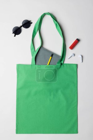 Téléchargez les photos : Vue grand angle du sac en toile verte avec ordinateur portable, lunettes de soleil, écouteurs et briquet, espace de copie. Sacs et concept de mode. - en image libre de droit