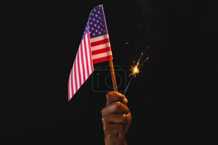 Téléchargez les photos : Main de l'homme biracial tenant drapeau des États-Unis d'Amérique et scintillant avec espace de copie. Patriotisme américain, fête de l'indépendance et concept de tradition. - en image libre de droit