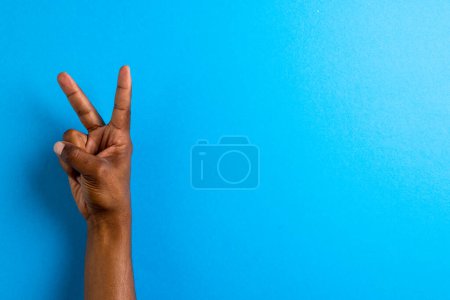 Téléchargez les photos : Gros plan de la main de l'homme biracial montrant signe de paix avec espace de copie sur fond bleu. Concept de mouvement pour la paix et contre la guerre. - en image libre de droit
