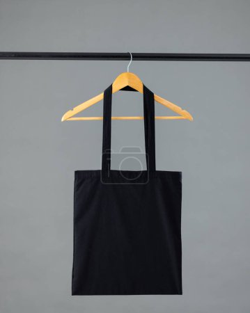 Photo for Close up of black canvas bag hanging on wooden clothes hanger with copy space on grey background. Eco friendly shopping bags and fashion concept. - Royalty Free Image