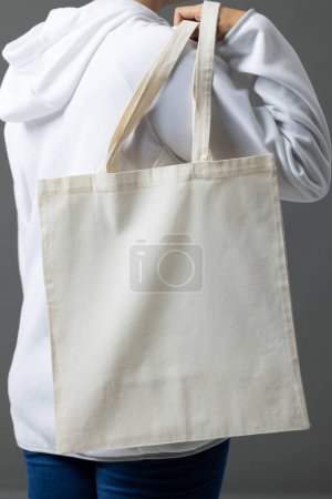 Foto de Mujer caucásica sosteniendo sobre el hombro bolsa de lona blanca con espacio de copia sobre fondo gris. Bolsas y concepto de moda. - Imagen libre de derechos