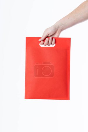 Téléchargez les photos : Main de femme caucasienne tenant sac rouge avec espace de copie sur fond blanc. Sacs et concept de mode. - en image libre de droit