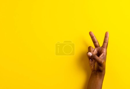 Foto de Primer plano de la mano del hombre biracial mostrando signo de paz con espacio de copia sobre fondo amarillo. Concepto de paz y movimiento contra la guerra. - Imagen libre de derechos