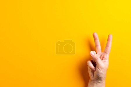 Téléchargez les photos : Gros plan de la main d'une femme caucasienne montrant un signe de paix avec un espace de copie sur fond jaune. Concept de mouvement pour la paix et contre la guerre. - en image libre de droit