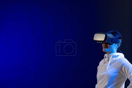 Foto de Mujer asiática feliz usando auriculares vr en estudio con luz azul con espacio de copia. Realidad virtual y tecnología de interfaz digital. - Imagen libre de derechos