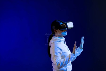Photo for Asian woman using vr headset in studio with blue light with copy space. Virtual reality and digital interface technology. - Royalty Free Image