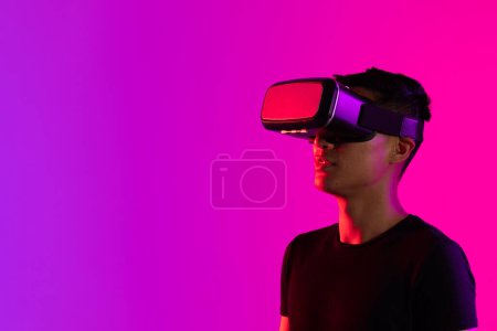 Photo for Asian man using vr headset in studio with purple light and copy space. Virtual reality and digital interface technology. - Royalty Free Image
