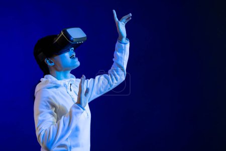 Foto de Mujer asiática usando auriculares vr en estudio con luz azul con espacio de copia. Realidad virtual y tecnología de interfaz digital. - Imagen libre de derechos