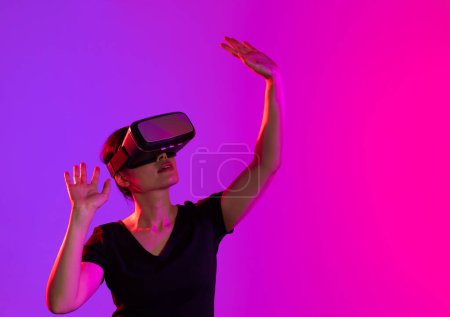 Téléchargez les photos : Femme asiatique utilisant un casque vr en studio avec lumière rose et bleue et espace de copie. Réalité virtuelle et technologie d'interface numérique. - en image libre de droit