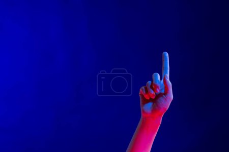 Exposed hand pointing finger in studio with blue light with copy space. Virtual reality and digital interface technology.