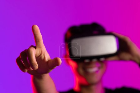 Foto de Feliz hombre asiático usando auriculares vr en estudio con luz púrpura y espacio de copia. Realidad virtual y tecnología de interfaz digital. - Imagen libre de derechos