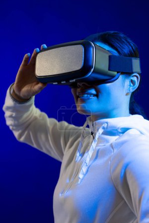 Téléchargez les photos : Heureuse femme asiatique tenant vr casque en studio avec lumière bleue. Réalité virtuelle et technologie d'interface numérique. - en image libre de droit