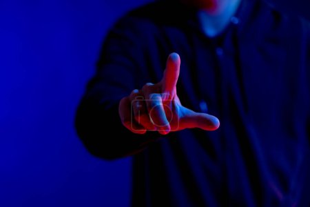 Foto de Hombre asiático señalando con el dedo en el estudio con luz azul con espacio de copia. Realidad virtual y tecnología de interfaz digital. - Imagen libre de derechos