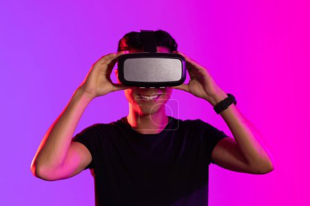 Téléchargez les photos : Portrait d'homme asiatique heureux utilisant un casque vr en studio avec une lumière violette et un espace de copie. Réalité virtuelle et technologie d'interface numérique. - en image libre de droit