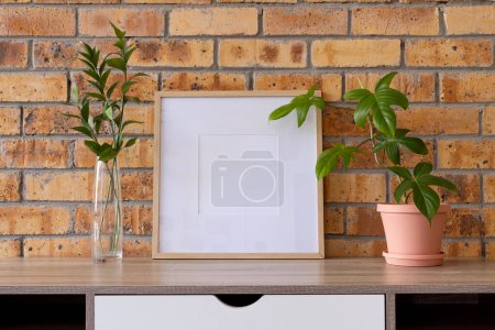 Photo for Wood empty frame with copy space and plants in pots on desk against brick wall. Mock up frame template, interior design and decoration. - Royalty Free Image