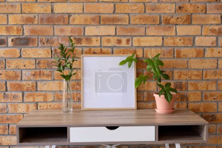 Photo for Wood empty frame with copy space and plants in pots on desk against brick wall. Mock up frame template, interior design and decoration. - Royalty Free Image